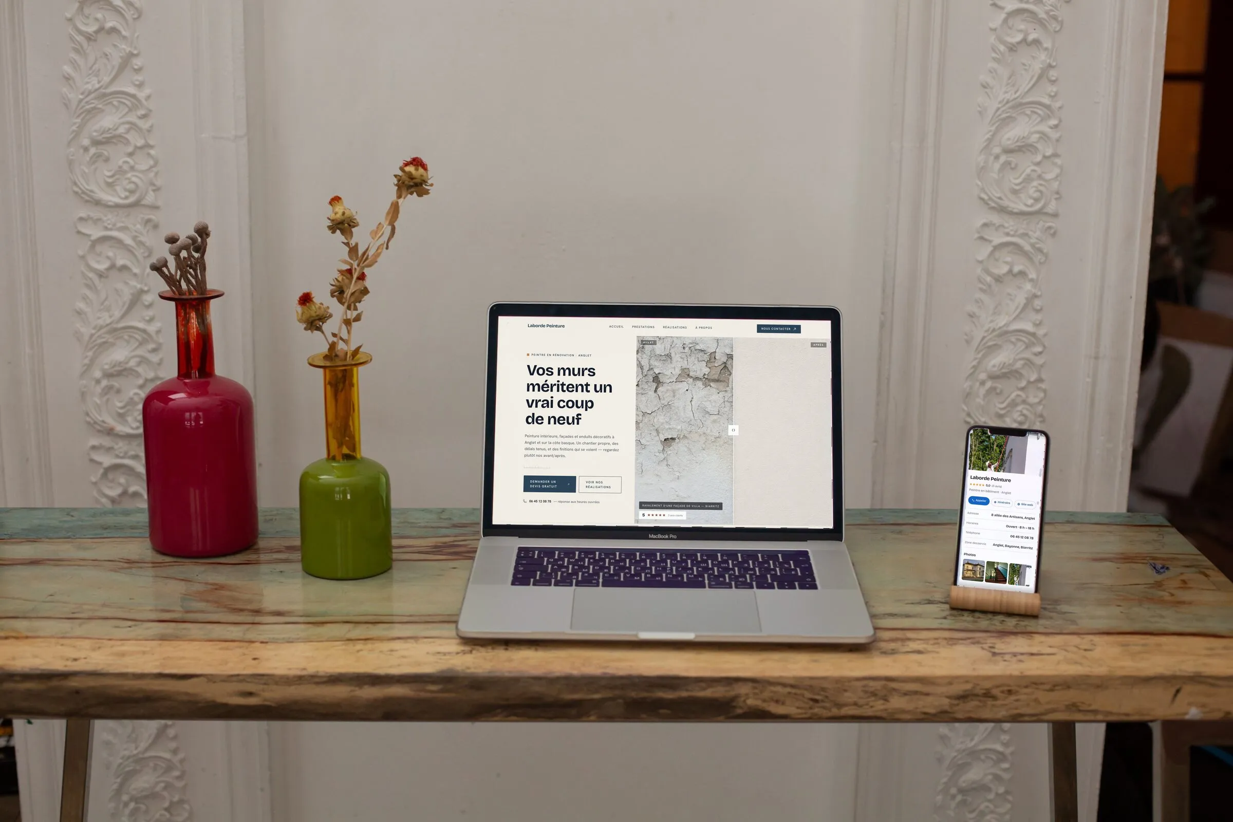 Un ordinateur et un téléphone qui affichent un site que nous avons fait, posés sur une console patinée entre deux vases.