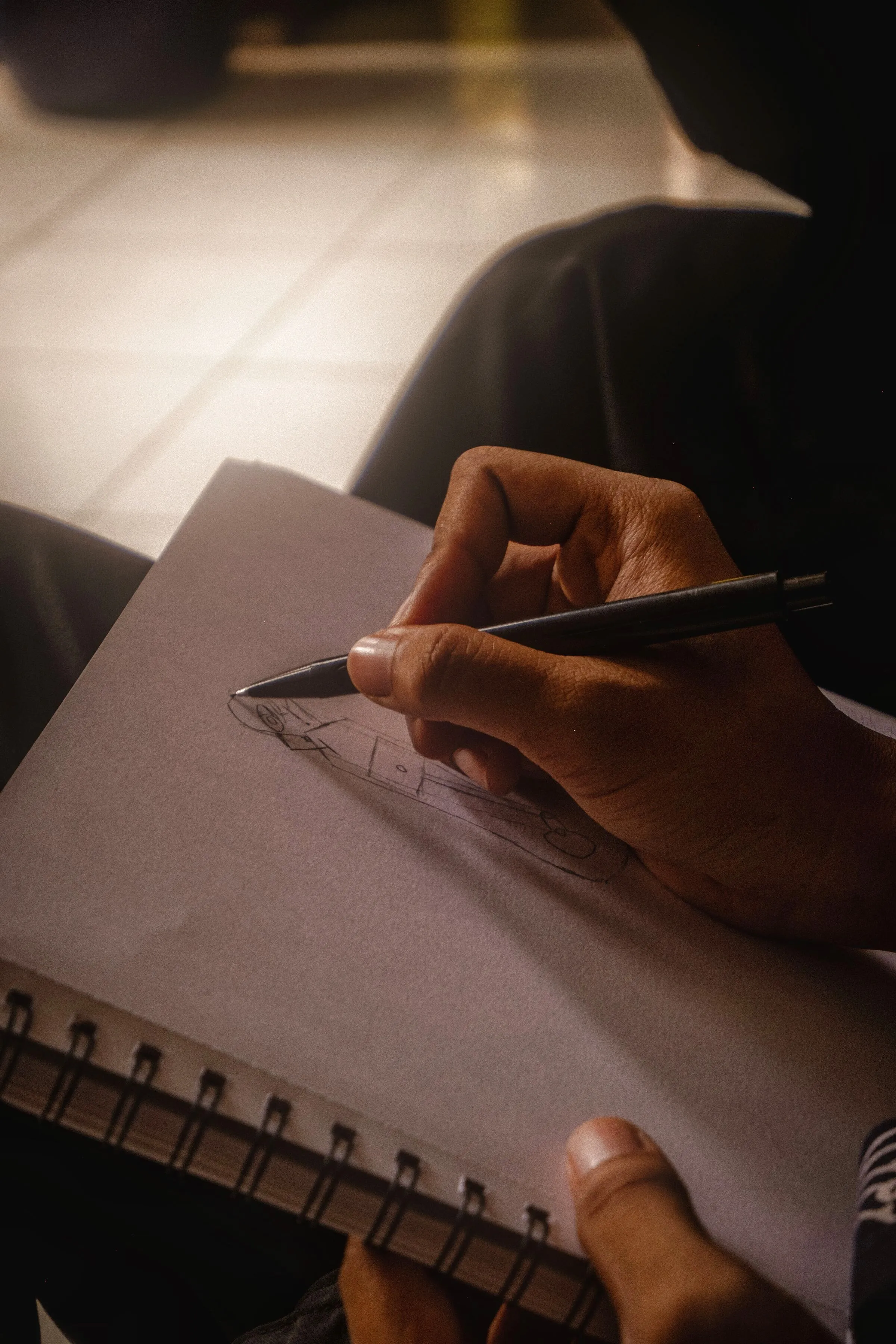 Une main qui écrit au stylo sur un carnet, dans une lumière chaude.