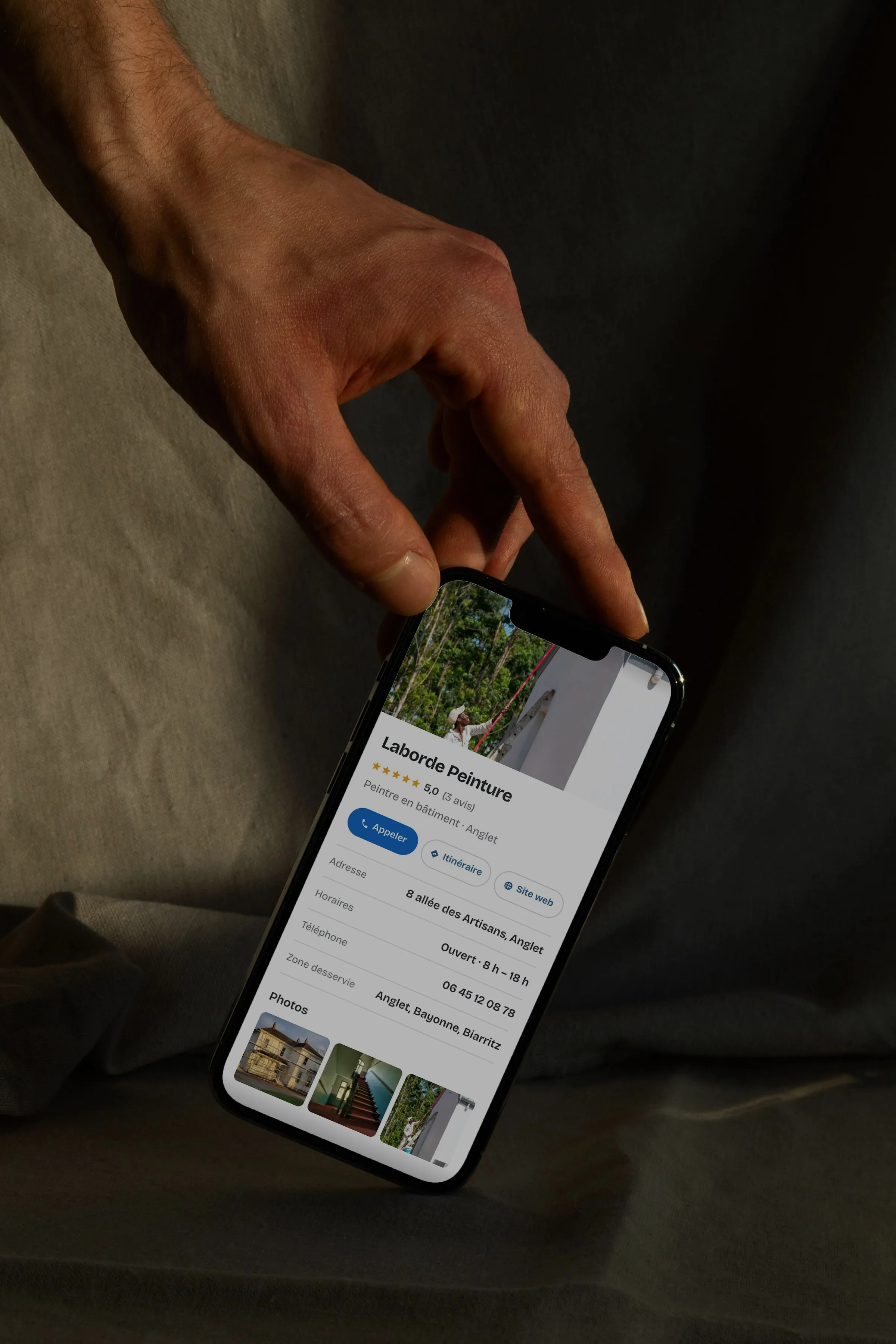 Une fiche d’établissement affichée sur un téléphone tenu à la main : nom, note, horaires, zone desservie et photos.
