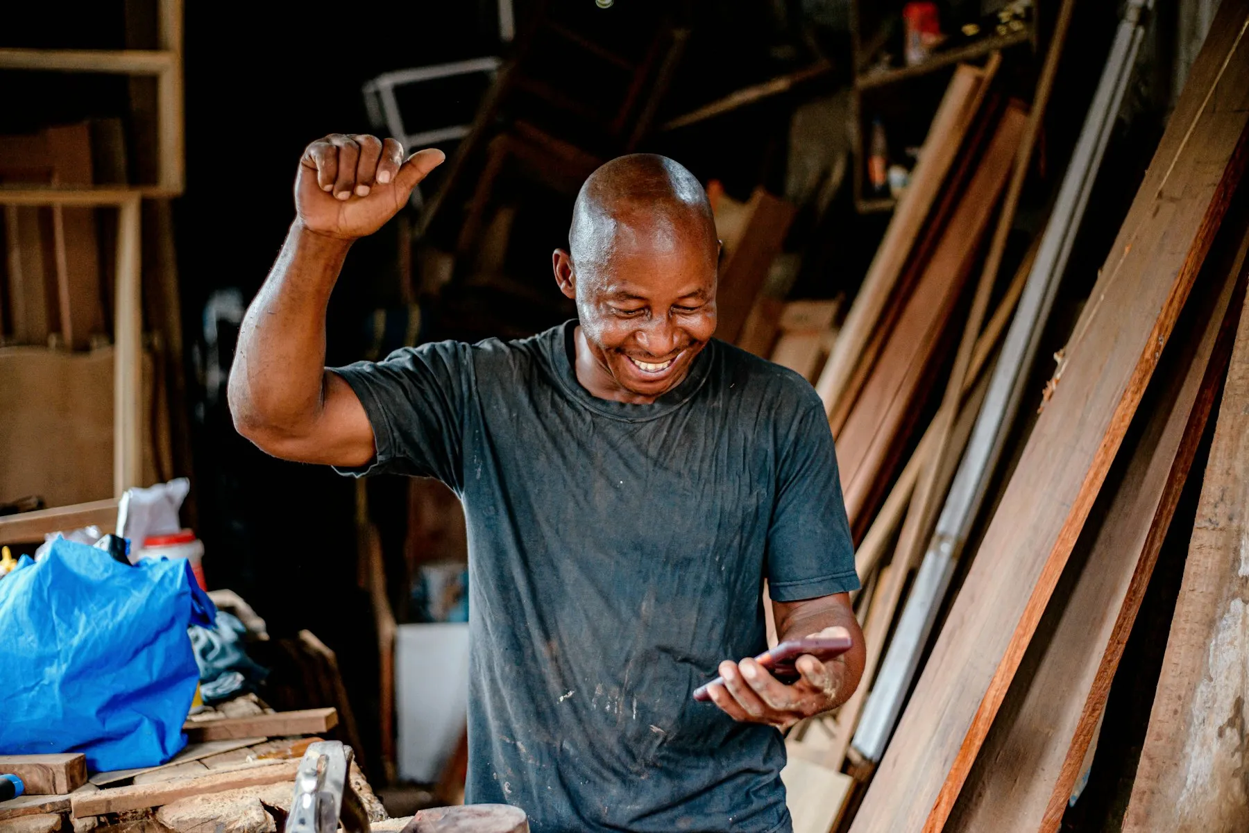 Un menuisier consulte son téléphone dans son atelier, le sourire aux lèvres