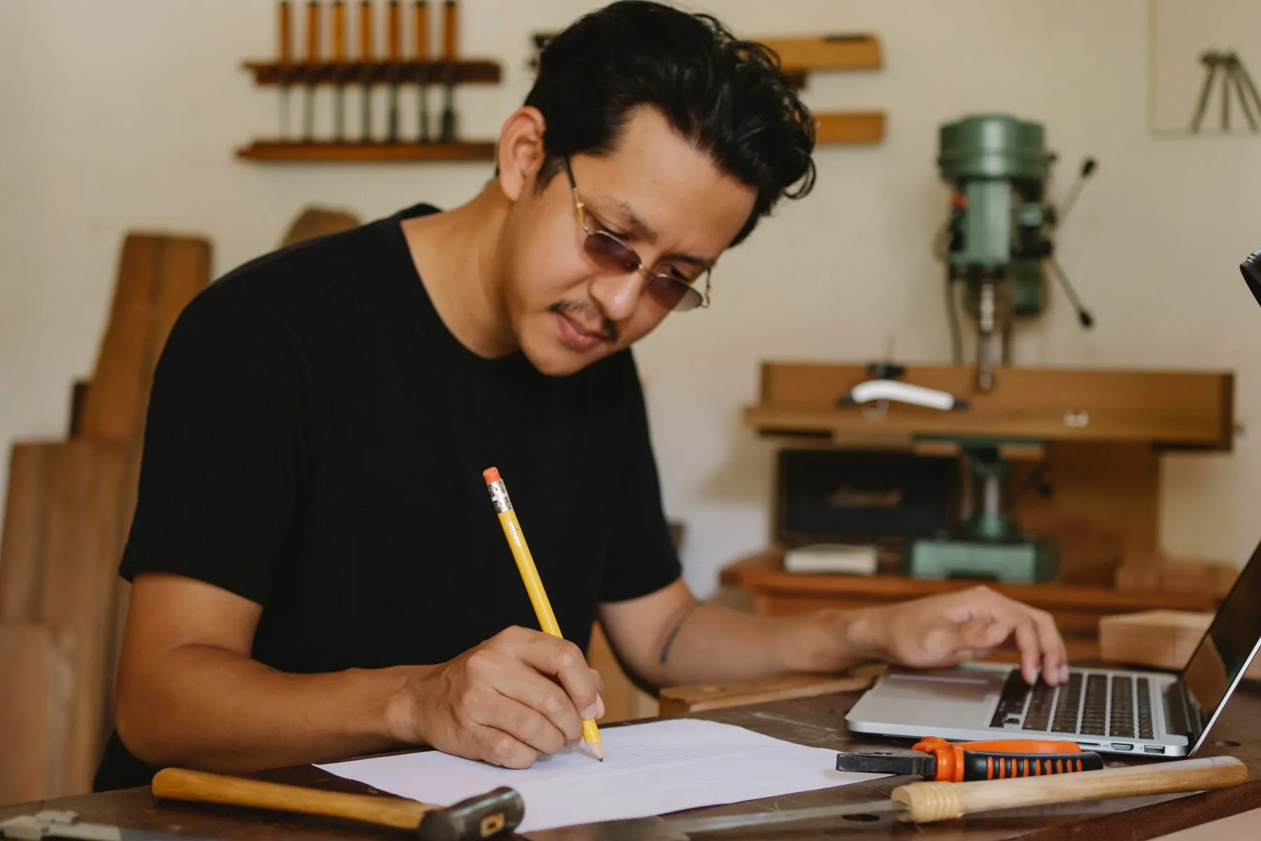 Un artisan note quelque chose au crayon, son ordinateur portable ouvert à côté de lui