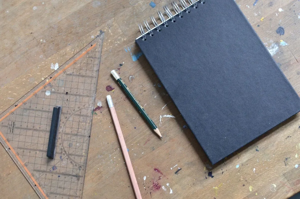 Un carnet noir, des crayons et une équerre posés sur un établi.