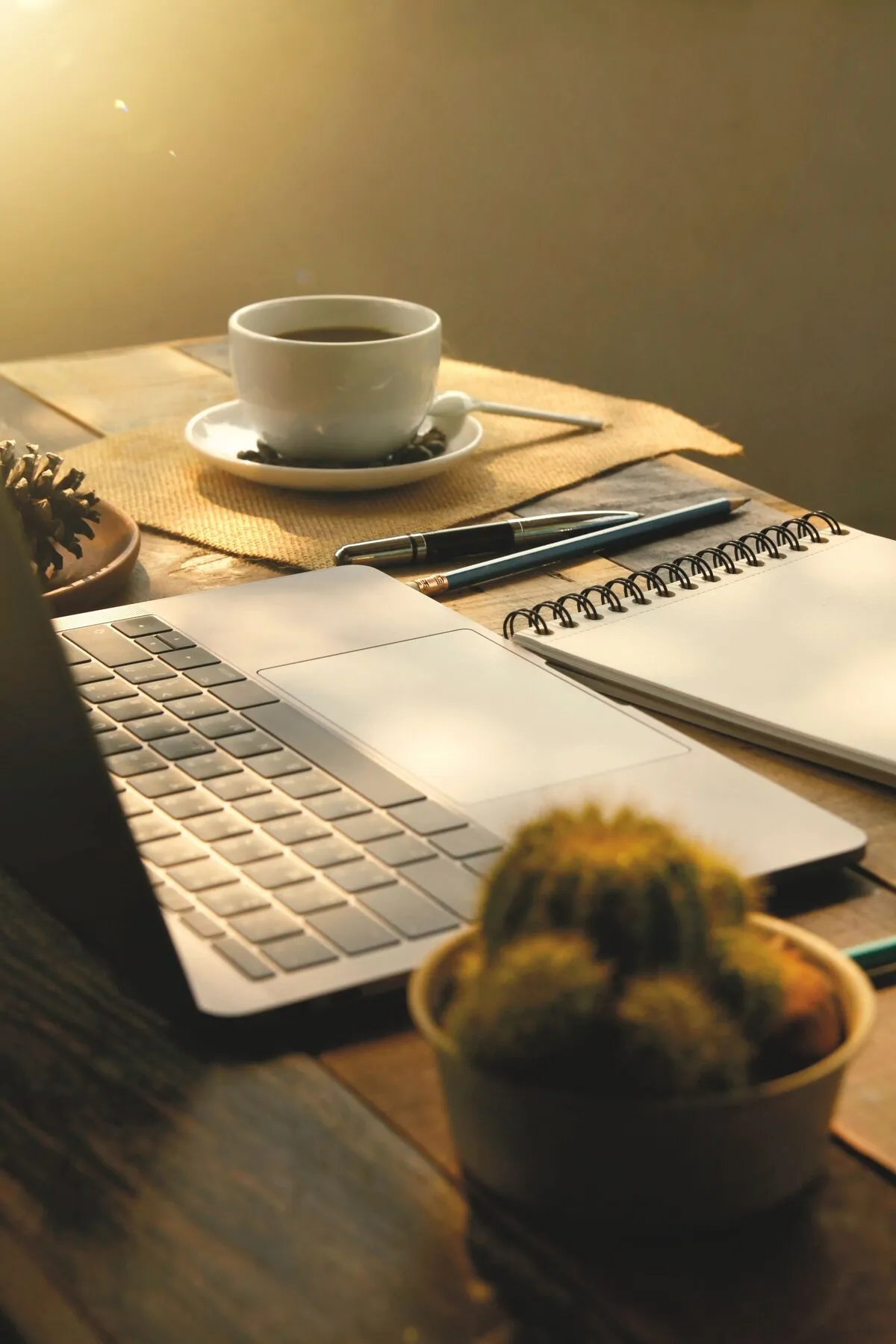 Un ordinateur portable ouvert, un carnet et une tasse dans la lumière du matin.