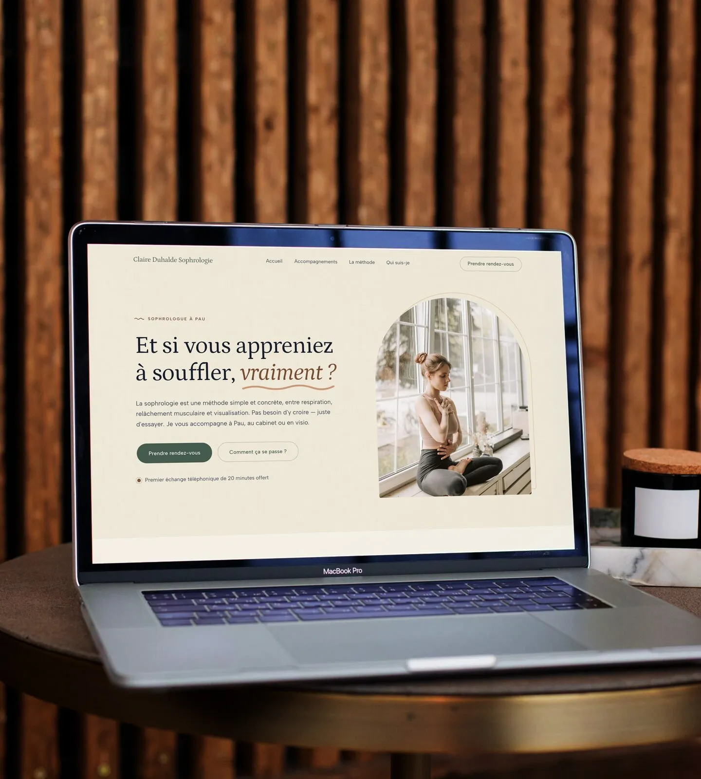 Le site d’une sophrologue ouvert sur un ordinateur portable, posé sur une table ronde devant un mur de tasseaux de bois